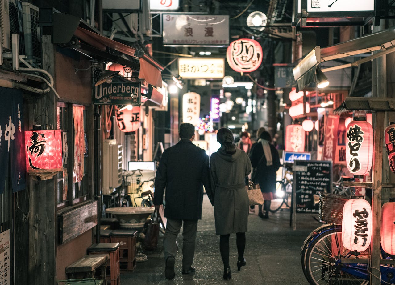 Couple strolling through Osaka's bustling alley at night, surrounded by glowing lanterns and shop signs.