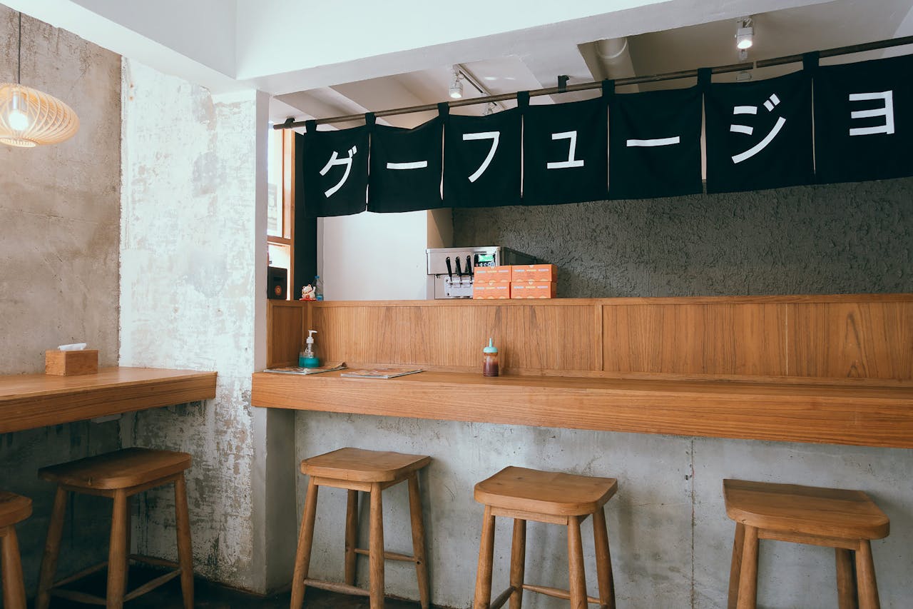 Warm and contemporary izakaya interior showcasing wooden stools and a minimalist bar setting.